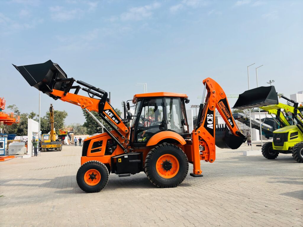 pexels-photo-29827751 Bright orange ACE AX 124 backhoe loader on display at an outdoor exhibition in India.